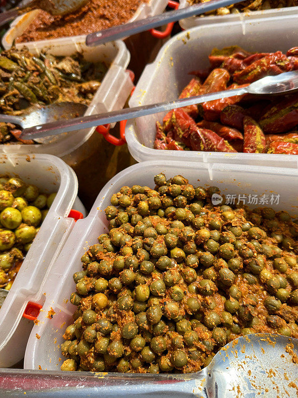 食品市场摊位的特写图像，展示了一排排塑料盒子，里面有泡菜和酸辣酱，金属勺子，填充红辣椒，tenti dela和kerda泡菜，高架视图，重点在前景